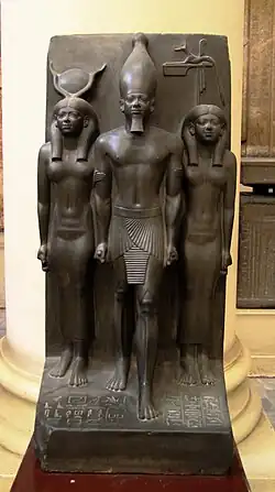 Triade du 17e&nbsp;nome, Cynopolis, nome du Chacal. Le personnage du nome passe son bras dans le dos du roi. 92,5&nbsp;×&nbsp;43&nbsp;cm. Musée du Caire JE 40679