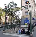 Photographie d'une bouche de métro d'où sortent, au premier plan deux hommes portant des chemises à manches courtes, un troisième se tenant debout sur les premières marche et téléphonant.