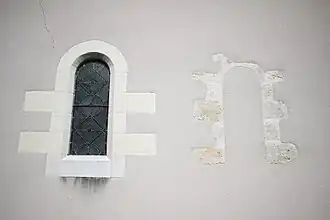 Photographie en couleurs d'un mur percé de deux fenêtres, l'une murée.