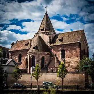Photographie d'un bâtiment en pierre avec une tour centrale et des toits pointus se trouvant au bord d'un quai dans une ville.
