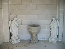 Une ancienne cuve baptismale en pierre entourée de deux statues d'anges.