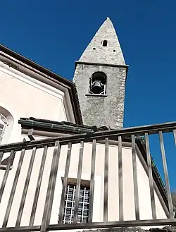 Photographie d'un clocher d'église gris et assez simple, avec une barrière en métal devant.