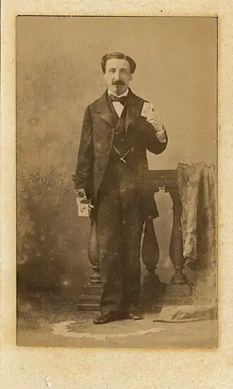 Élie Cabrol debout tenant des cartes à jouer