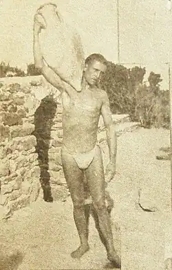 Photographie noir et blanc. Homme en maillot de bain portant sur son épaule une amphore.