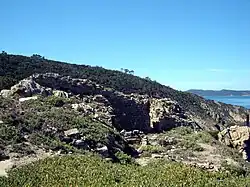 Photographie couleur de ruines dans la garigue. La mer semble surplomblée.
