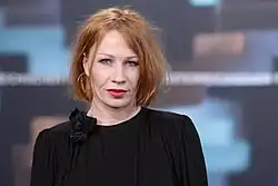 Photographie en couleur en buste d'une femme aux cheveux roux et vêtue de noir.