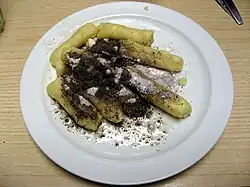 Dans une assiette blanche, quenelles de pommes de terre nappées de sucre fondant et de graines de pavot.