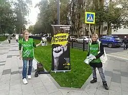 Photographie en couleurs de deux femmes portant des T-shirts verts et distribuant des tracts en ville.