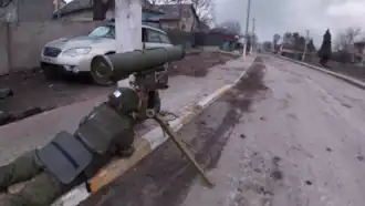 Photo couleur d'un soldat allongé sur un trottoir en train de manipuler un lance-missile monté sur trépied.