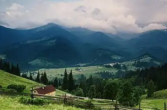 Paturages et forêt en montagne, dans les près quelques maisons éparses, une clôture.