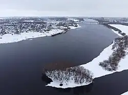 Photographie aérienne hivernale de la rivière Volkhov, avec en arrière-plan le pont de Deverianitsy. Sur les rives, l'on distingue des maisons individuelles et des bâtiments soviétiques.