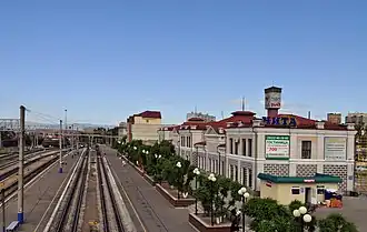 Photographie prise depuis une passerelle piéton au-dessus de vois ferroviaires prenant un bâtiment à côté de quais de gare.