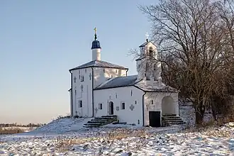 Photographe d'une église blanche orthodoxe avec un toit bleu, entourée d'un espace enneigé.