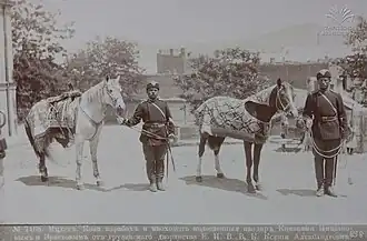 Photographie sepia de deux chevaux harnachés et deux militaires qui les tiennent