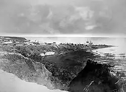 Photographie en noir et blanc d'un village sur un éperon rocheux au bord d'un lac.