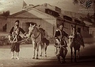 Photographie sepia de deux chevaux harnachés et deux militaires qui les tiennent