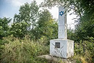 Monument blanc composé d'un socle rectangulaire et d'une obélisque. Deux écriteaux portent des inscriptions en hébreu et en ukrainien ; une étoile de David bleue est placardée en partie haute de l'obélisque.