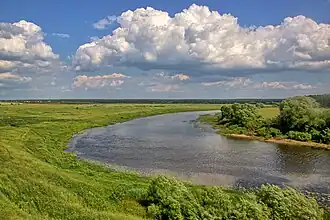 Paysage vert et plat traversée par une rivière faisant une méandre.