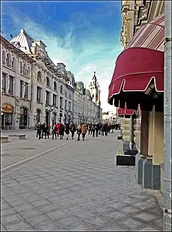 Vue actuelle de la rue bordée d'un bâtiment néo-classique en pierre gris pâle devant lequel passent des promeneurs