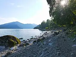 Plage de galets sur le lac avec des touristes (au fond).