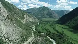 Photographie aérienne d'une vallée encaissée, avec la route longeant la rivière qui passe au centre. L'endroit est vert, avec des arbres recouvrant les pentes. La hauteur des montagnes est importante.