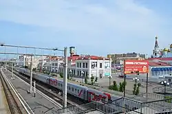 Photographie depuis une paserelle piétonne de trois quais d'une gare, dont un quai avec un chemin de fer gris à un étage. En arrière-plan se trouve un bâtiment classique de deux étages, la gare de Tchita II.