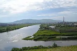 Photographie de la confluence d'une rivière large au centre avec une rivière plus petite en bas à droite. Sur la rive droite de la rivière large (l'Ingoda) se trouve une cheminée d'une usine. Les rives des rivières sont vertes avec des marécages.