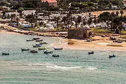 La plage et le village touristique. La ruine est l’ancienne douane, contre laquelle se trouve le potentiel charnier des victimes du massacre du 22 mai 1948.