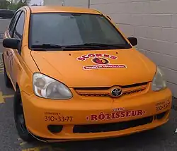 Voiture jaune avec écriture rouge sur le capôt stationné sur un terrain pavé avec un mur de béton à droite