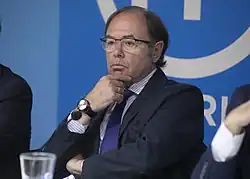 Photographie d'un homme brun, au front dégarni, portant des lunettes et assis.