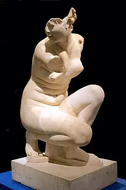 Vue de trois quart face sur le marbre d'une Aphrodite nue, sortant du bain accroupie. Le corps de face, visage tourné vers sa droite. Sur la pointe du pied droit, le gauche étant à plat. Fond noir. Marbre, H. 1,06&nbsp;m. Réplique romaine d'une statue originale hellénistique de la seconde moitié du IIIe&nbsp;siècle avant l'ère commune.