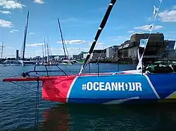 Gros plan de profil sur l'avant d'un voilier rouge, bleu et jaune, amarré à un ponton.