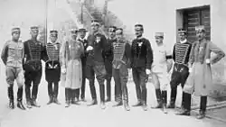 Photographie en noir et blanc représentant douze hommes en uniforme posant fièrement devant un bâtiment.