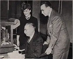 Deux personnes, debouts, derrière une autre, assise.