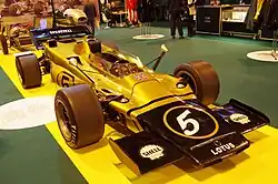 Photographie d'une monoplace de Formule 1 noire et or, vue de trois-quarts, dans un musée.