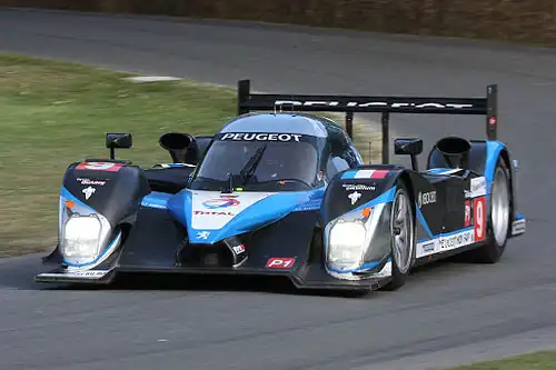Voiture d'endurance noire et bleu azur, vue de trois-quarts, à la sortie d'un virage.