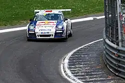 Porsche 997 GT3 Cup de couleur bleue et blanche, pilotée par Sébastien Loeb et vue de face dans un virage sur une piste goudronnée.