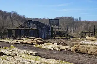 Un site défriché avec des tronc d’ares au premier plan et les ruines des bâtiments au second avec deux trémies de béton à l'arrière, l'une debout, l'autre sur le flanc.