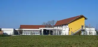 Un bâtiment à étage jaune et un bâtiment de plain-pied blanc encadrant une cours de récréation.