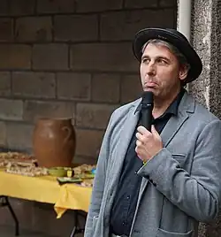 Portrait rapproché d'un homme portant une veste grise et un chapeau noir.