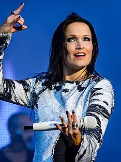 Image d'une femme brune habillée en noir et blanc et tenant un micro dans la main