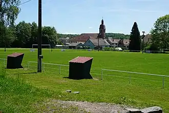 Un terrain de foot avec le village et le clocher à l'arrière-plan.