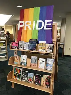 Illustration du Rainbow Book Month par un présentoir de livres sur le thème pour la Pride LGBTQ+ 2017, surmonté d’une tenture arc-en-ciel marquée « pride », à la bibliothèque publique Barbara S. Ponce de Pinellas Park en Floride.