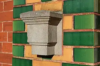 Briques jaunes, vertes et rouges et ancien support de marquise en pierre.