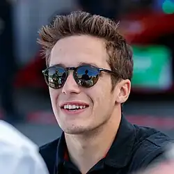 Photographie d'un jeune hommage de peau blanche, brun, en gros plan, souriant, de face, levant son trophée.