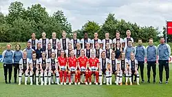 Photo de groupe de l'équipe d'Allemagne. Les joueuses sont photographiées en trois rangées, elles portent des maillots blancs avec une bande noire et leur numéros respectifs. Les gardiennes sont au centre au premier rang avec des maillot rouge portant des numéros jaunes. Le staff est situé de part et d'autre du rang central, avec des survêtements bleus.