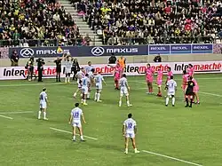 Photographie de plusieurs sportifs masculins durant un match avec le public en arrière-plan.