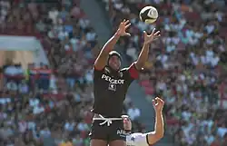 Joueur en l'air, tendant les deux bras en avant pour prendre un ballon en touche.