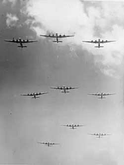 Photographie noir et blanc de bombardiers en formation dans le ciel (vue depuis le sol).