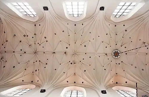 Photographie en contre-plongée d'une voûte blanche à nervures décorée d'étoiles.